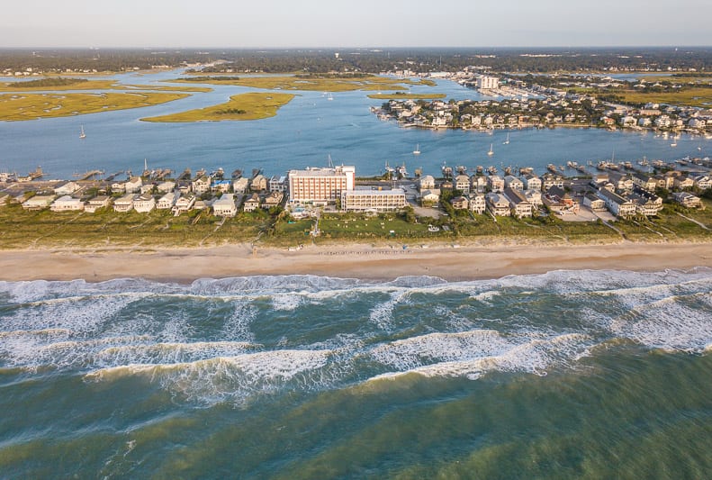 an aerial view of wrightsville Island with buildings and  the beach on one side and the sound on the other 