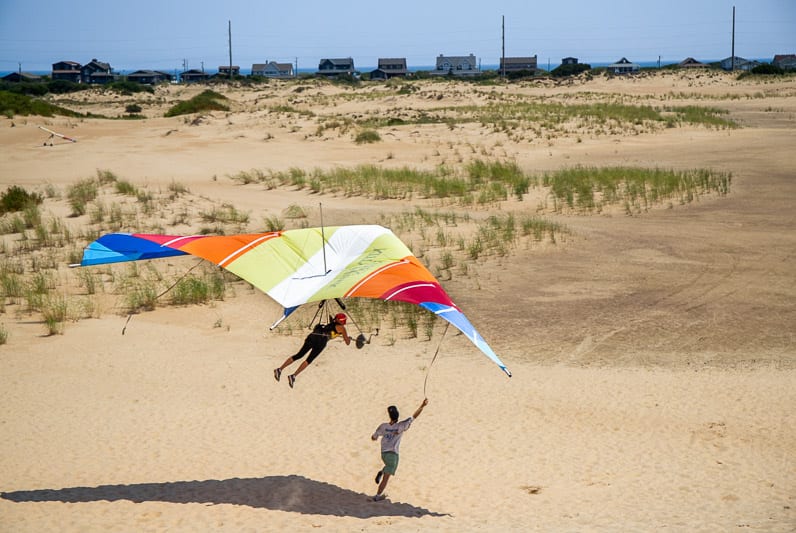 woman hang gliding with man running beside her