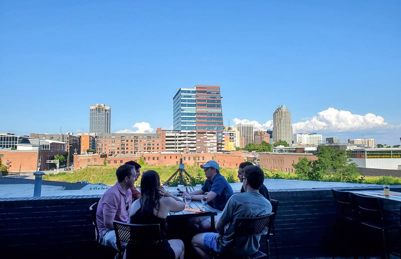 group of people sitting at table with view of raleigh skyline behind them