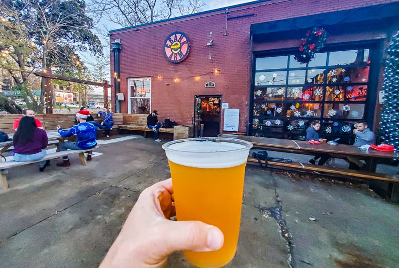 Hand holding a cup of beer in front of Crank Arm Brewing