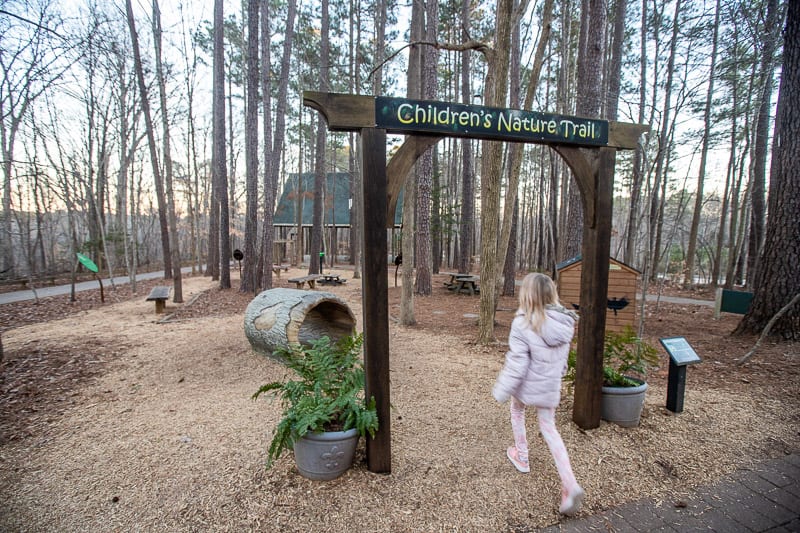 girl walking underneath a sign in a wooded area