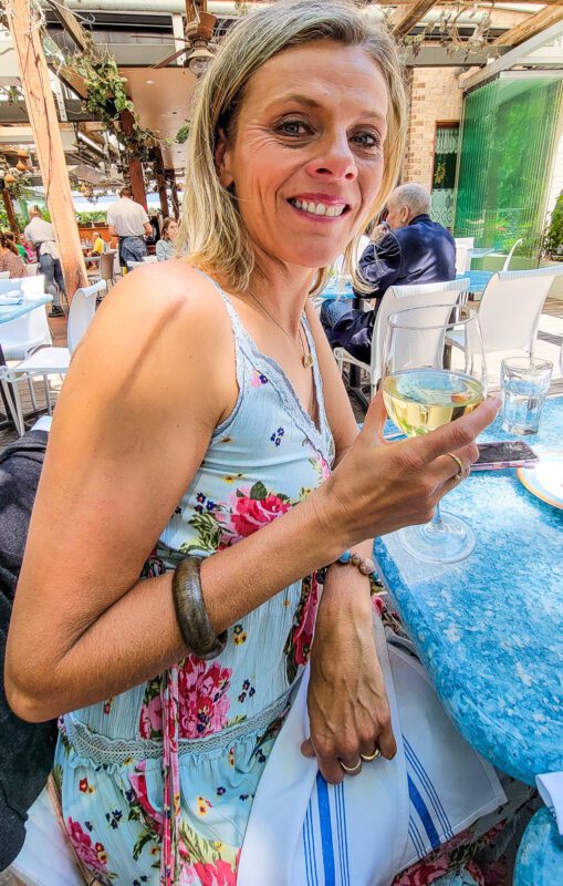 a woman smiling at the camera while holding a glass of wine