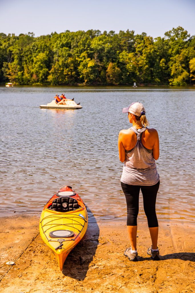 A person standing next to a body of water with a kayak