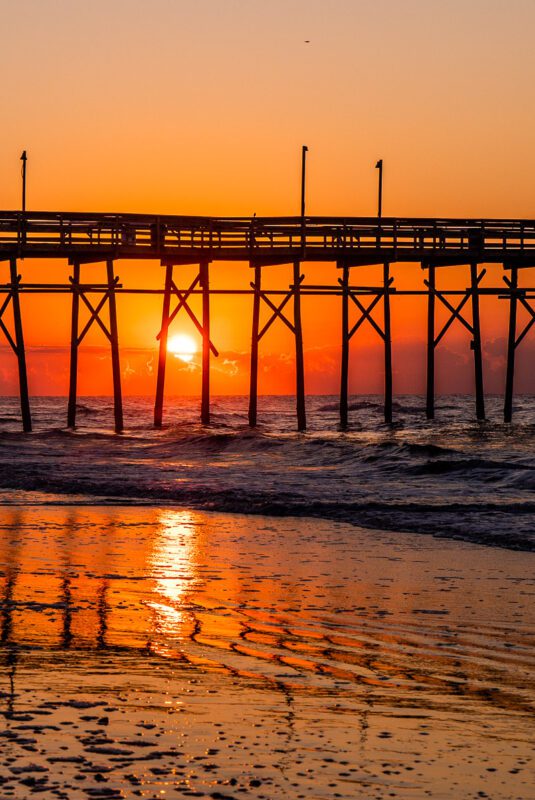 orange skies and sunrise between pier legs on Ocean Isle Beach