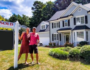 a couple standing in front of a house with a "sold" sign