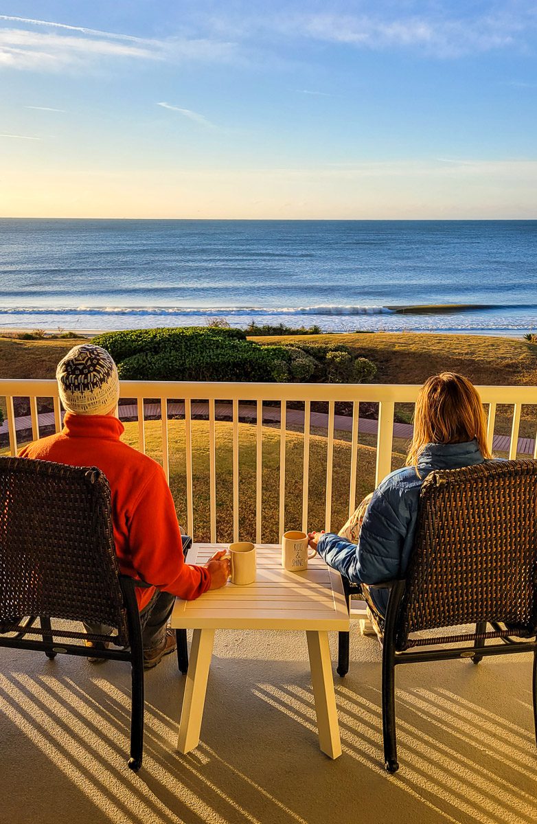 man and woman drinking coffee on balcony looking over the ocean