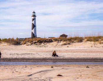 A girl sitting on a beach with a lighthouse in the background