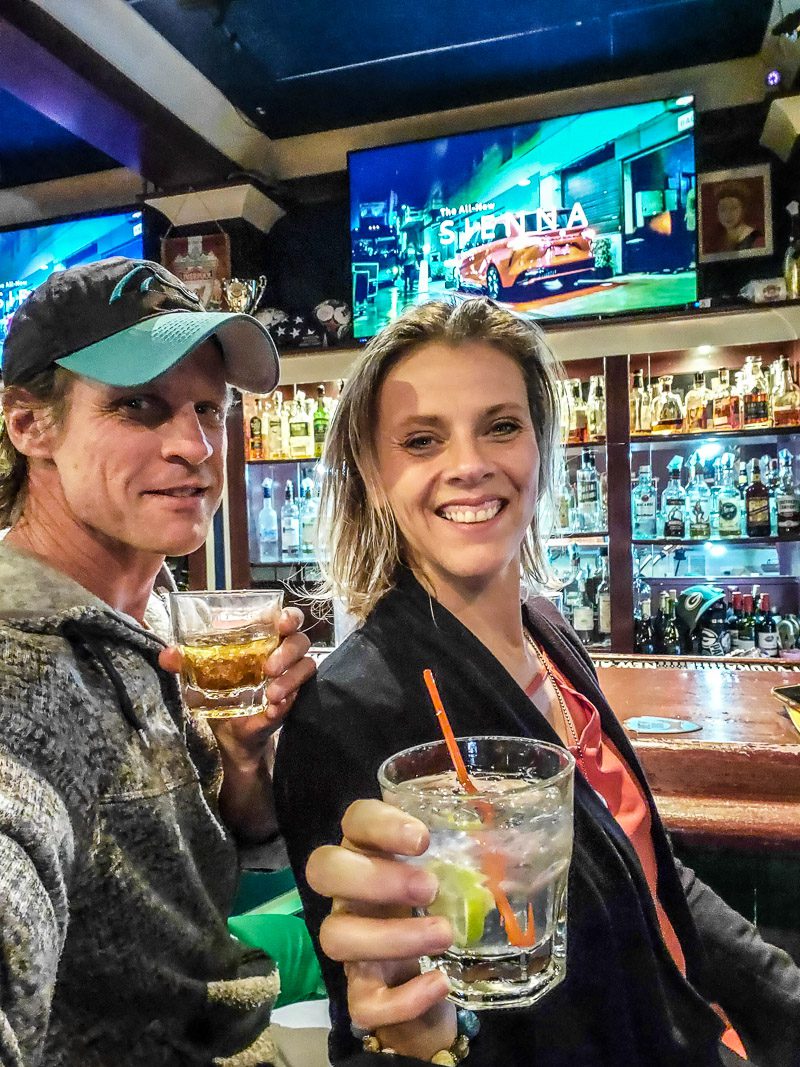 people smiling at the camera while holding drinks in front of a bar