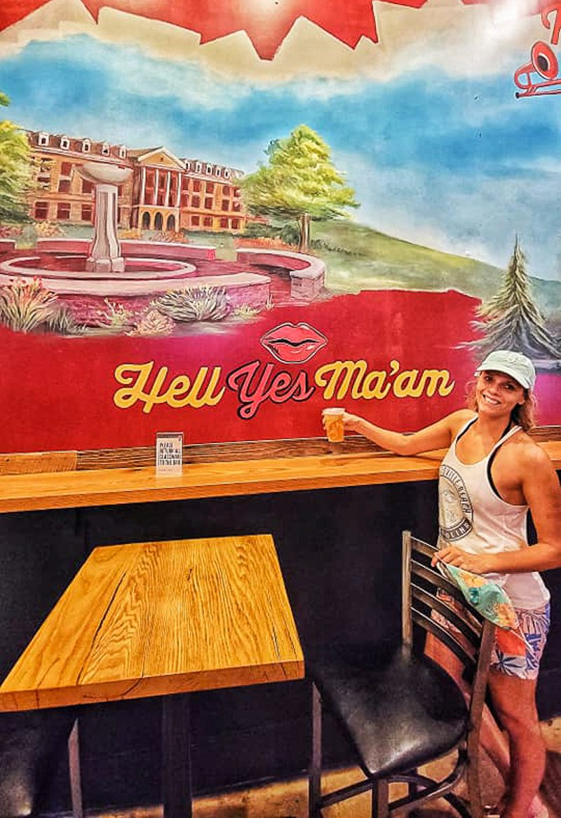 Woman holding a beer posing in front of a sign