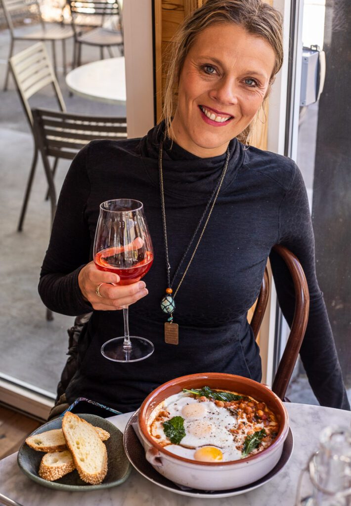 woman smiling at camera with mimosa in hand and plate of food on table Rosewater Kitchen, North Hills, Raleigh