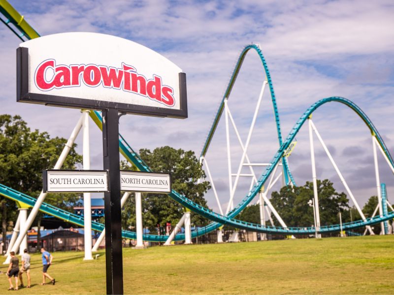 Blue roller coaster behind a sign for carowinds amusument park north and south carolina