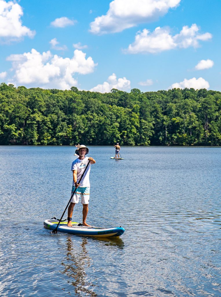 Man riding a stand up paddle board on Lake Johnson in Raleigh