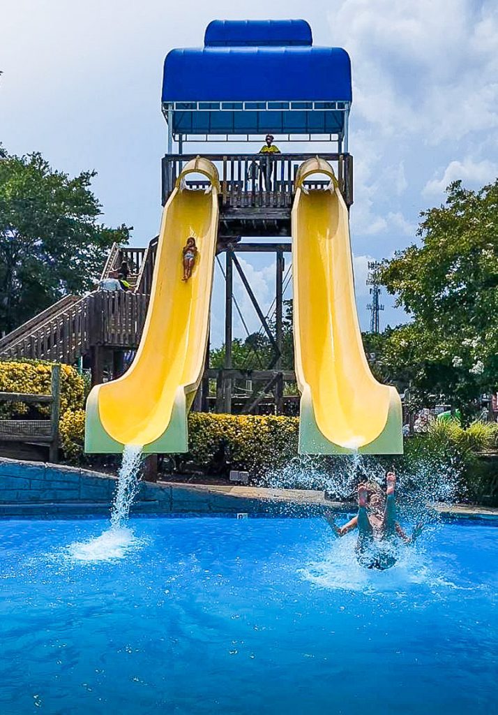 two people coming down twin yellow waterslides in A blue pool of water Wet\'n Wild Greensboro