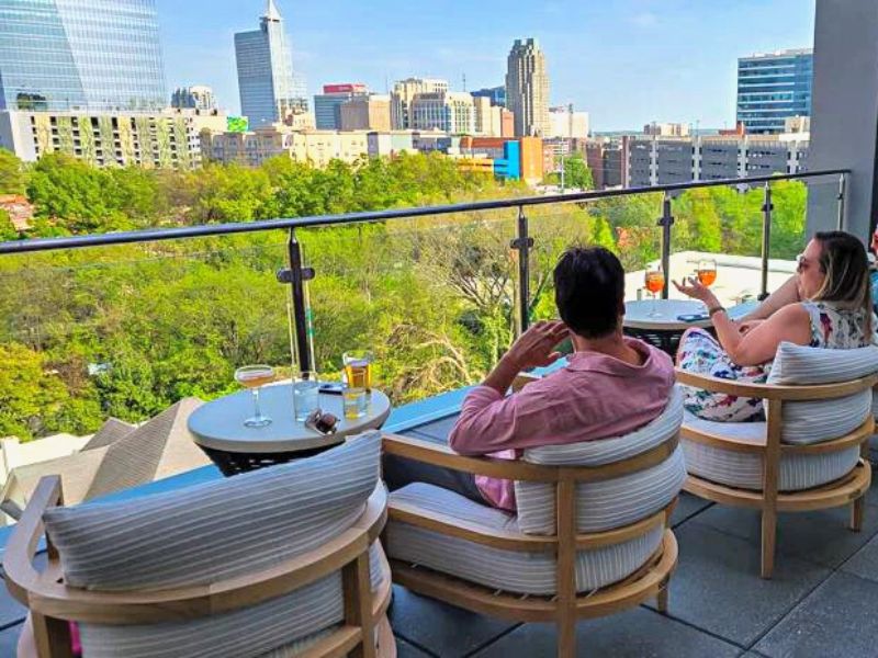 People having drinks at a rooftop bar with city skyline views of Raleigh, NC
