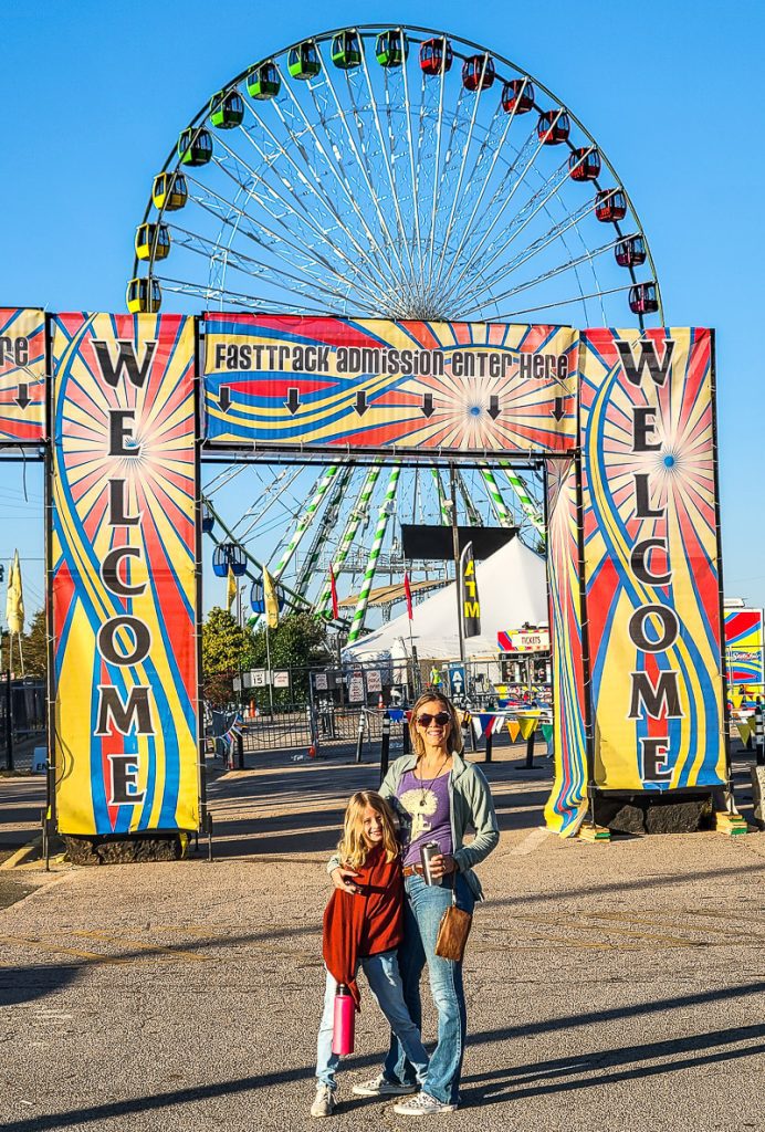Mother and daughter standing in front of a ferris wheel and entrance gat to the North Carolina State Fair