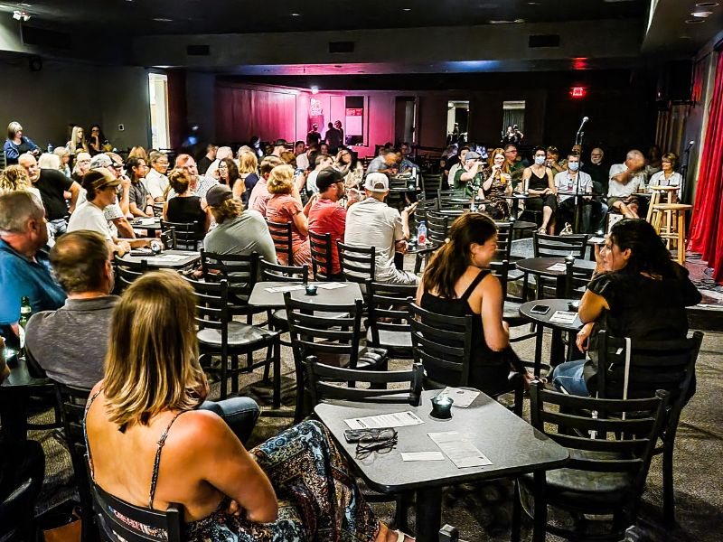 People sitting at tables and chairs inside a comedy club