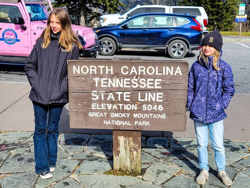 Two sisters standing next to a sign on the state border of North Carolina and Tennessee