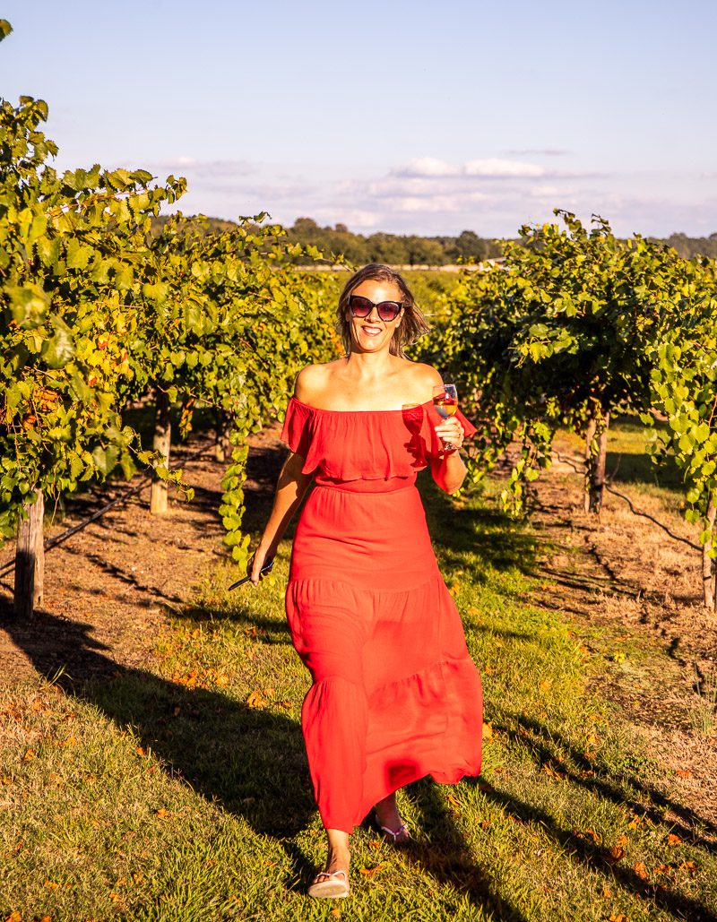 lady walking trhough a vineyard holding a glass of wine
