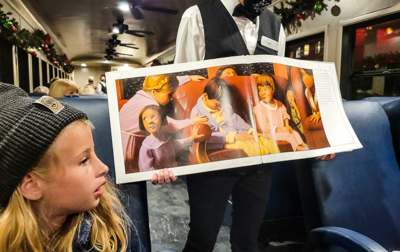 conductor showing pictures from the Polar Express book to young girl on the train