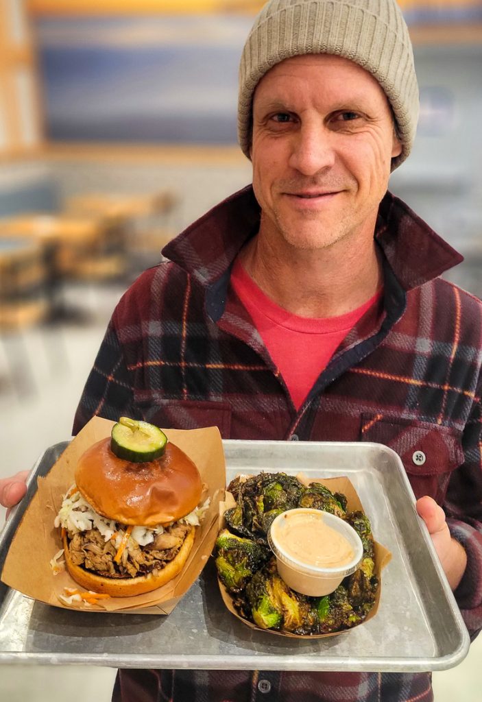 Man holding a tray with a burger and brussel sprouts