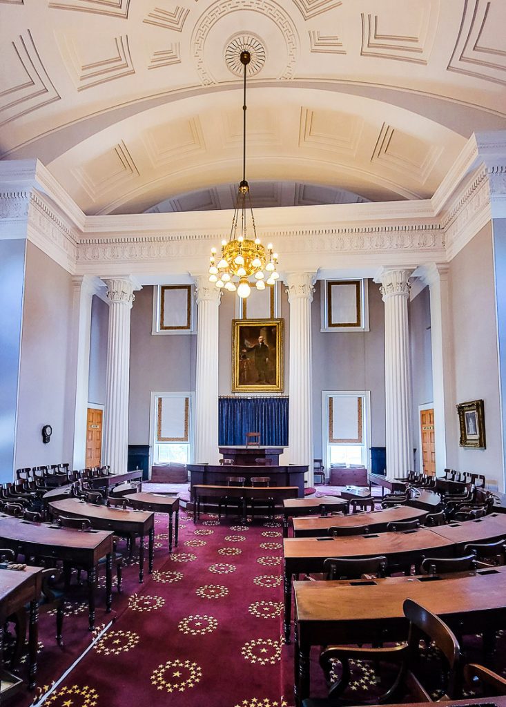 Inside of a state capitol building showing the chamber with tables and chairs