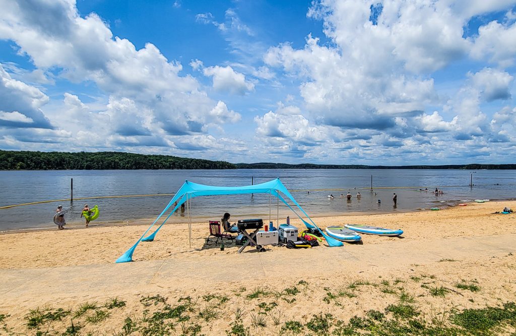 Sandy beach at a lake with people sitting under a sun shade