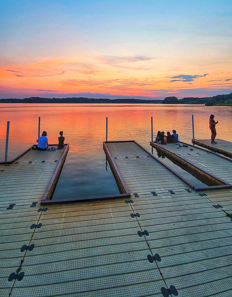 People sitting on a dock at a lake watching the sunset