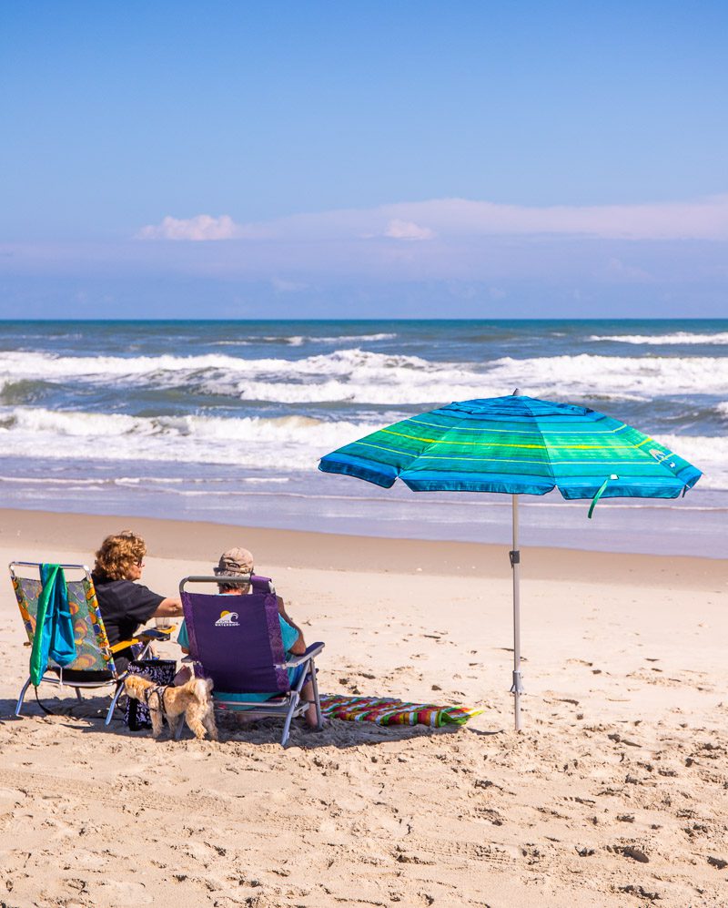 Man and woman sitting on beach chairs next to an umbrella on a beach on Ocracoke Island