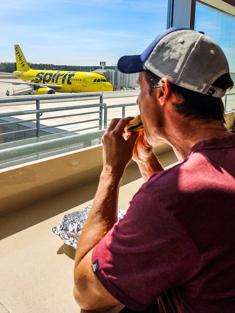 Man eating a burger at airport looking at a plane