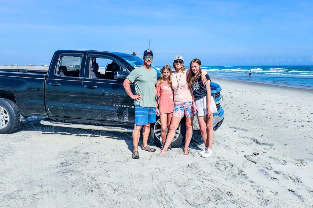 people standing next to car on the beach