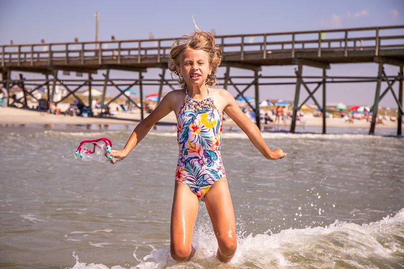 girl jumping out of water with pier behind her