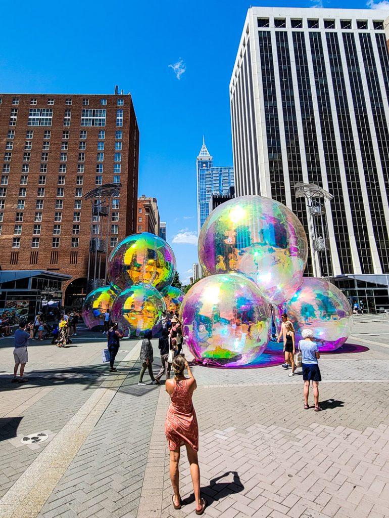 Woman taking a photo of colorful giant balls in a city street