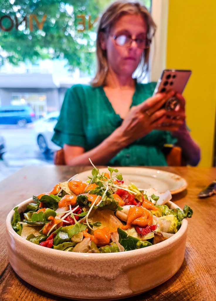Bowl of salad and lady taking a photo