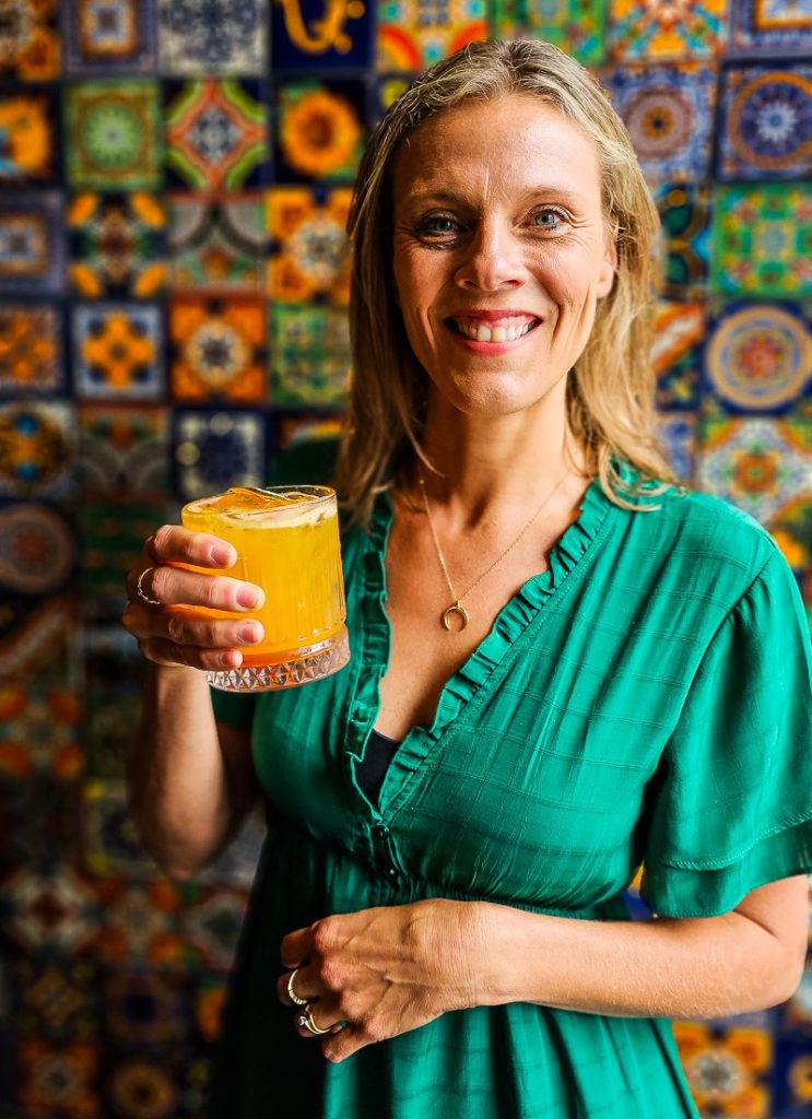 Lady holding a cocktail in her hands with mosaic tile background