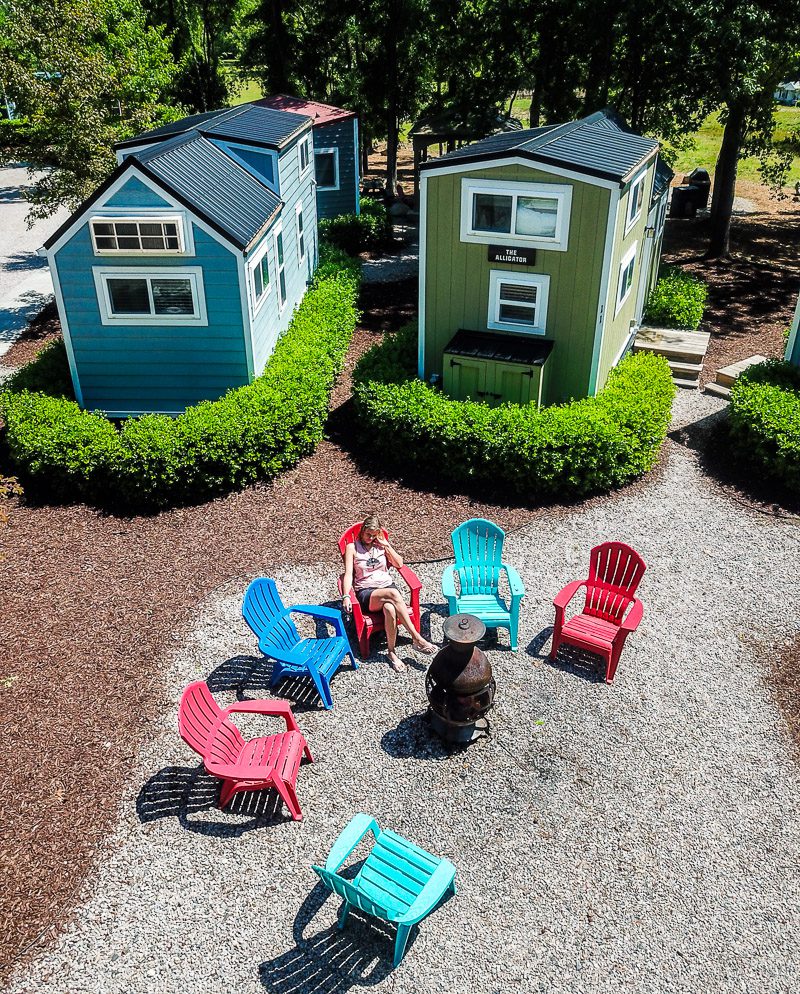 Aerial drone photo of lady sitting in chairs around camp fire and tiny home community