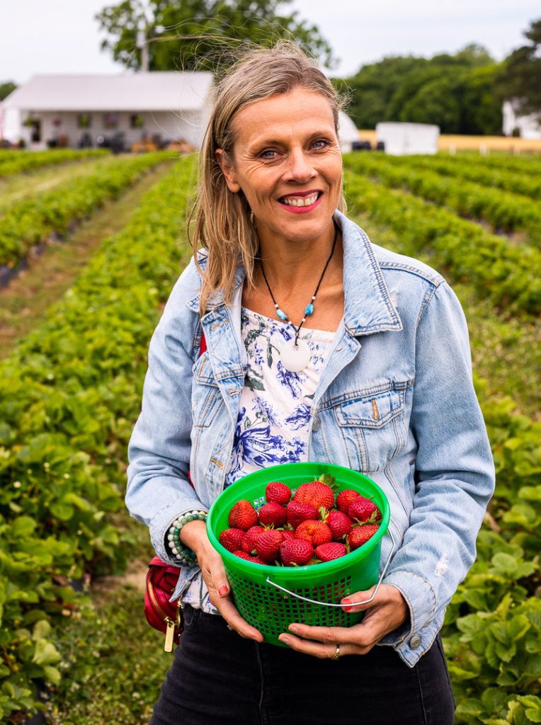 Caroline Makepeace (a woman) holding a bucket of strawberries in a field