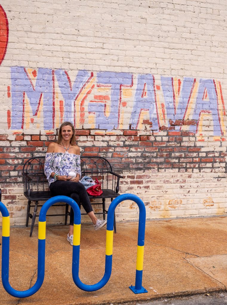 Caroline Makepeace sitting in front of a mural that says "My Java"