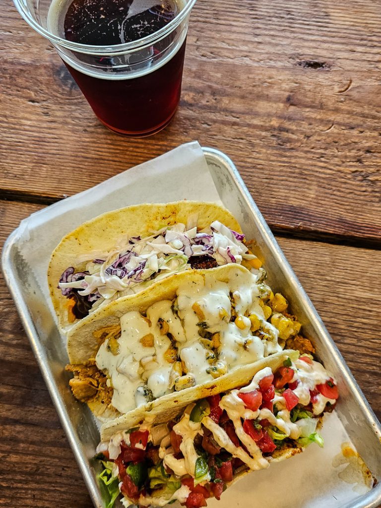 Three tacos on a plate and a beer