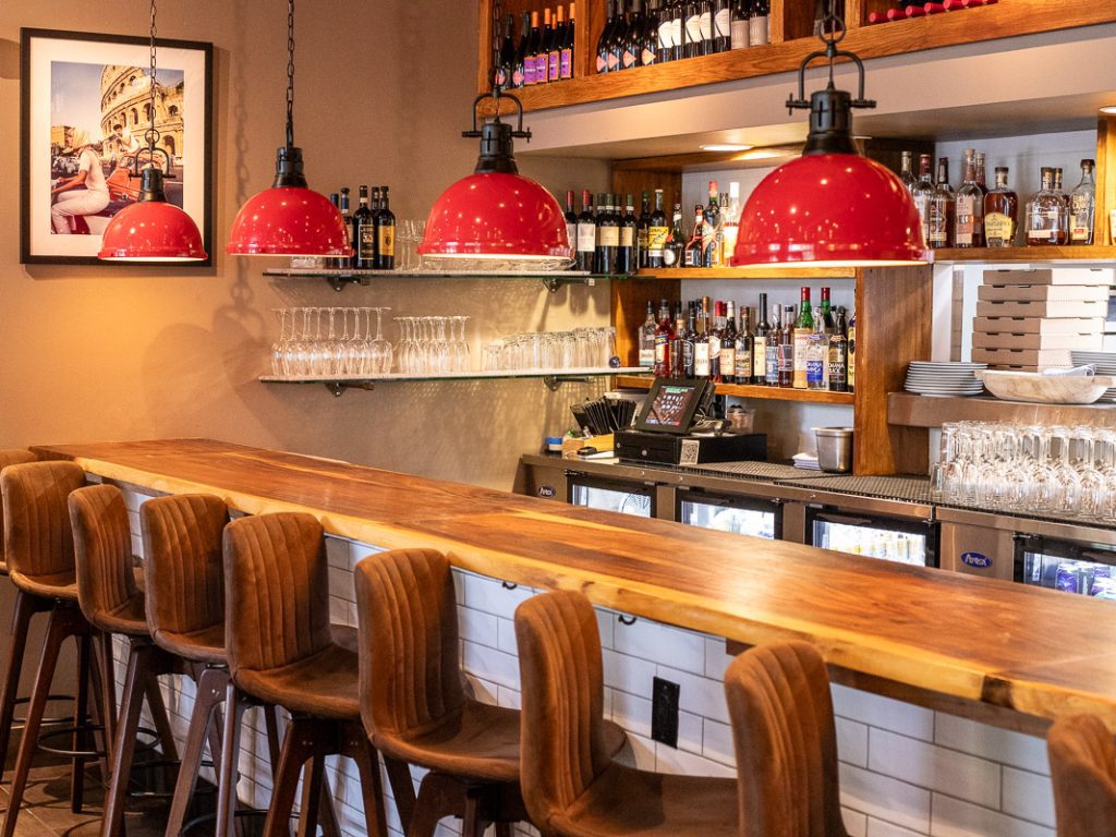 Chairs at a bar with wine on shelves and red lamps