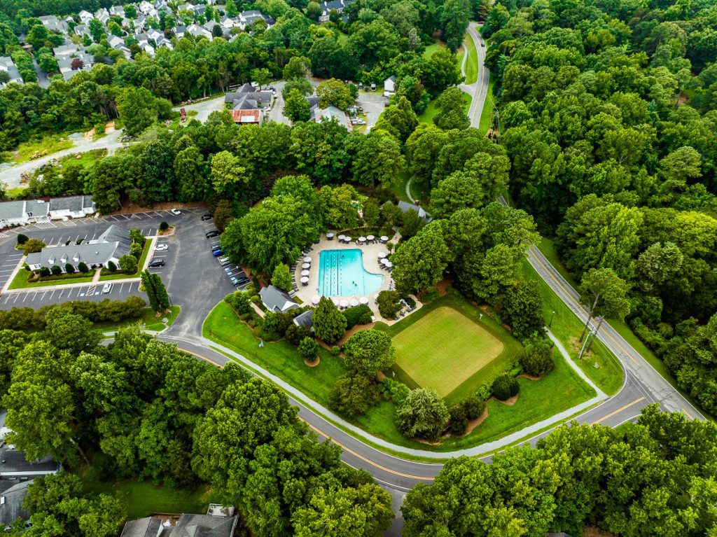 Aerial photo of a swimming pool surrounded by green trees and a road