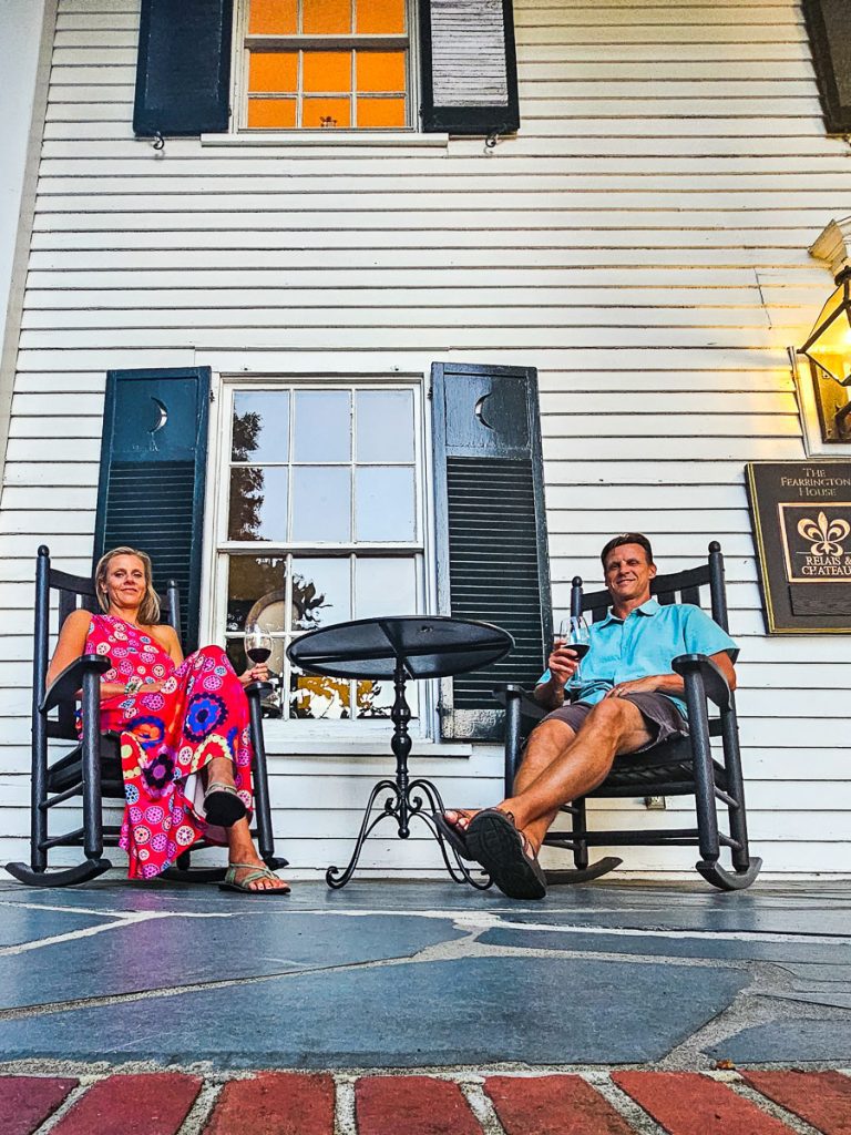 Man and woman sitting in chairs on a porch drinking wine
