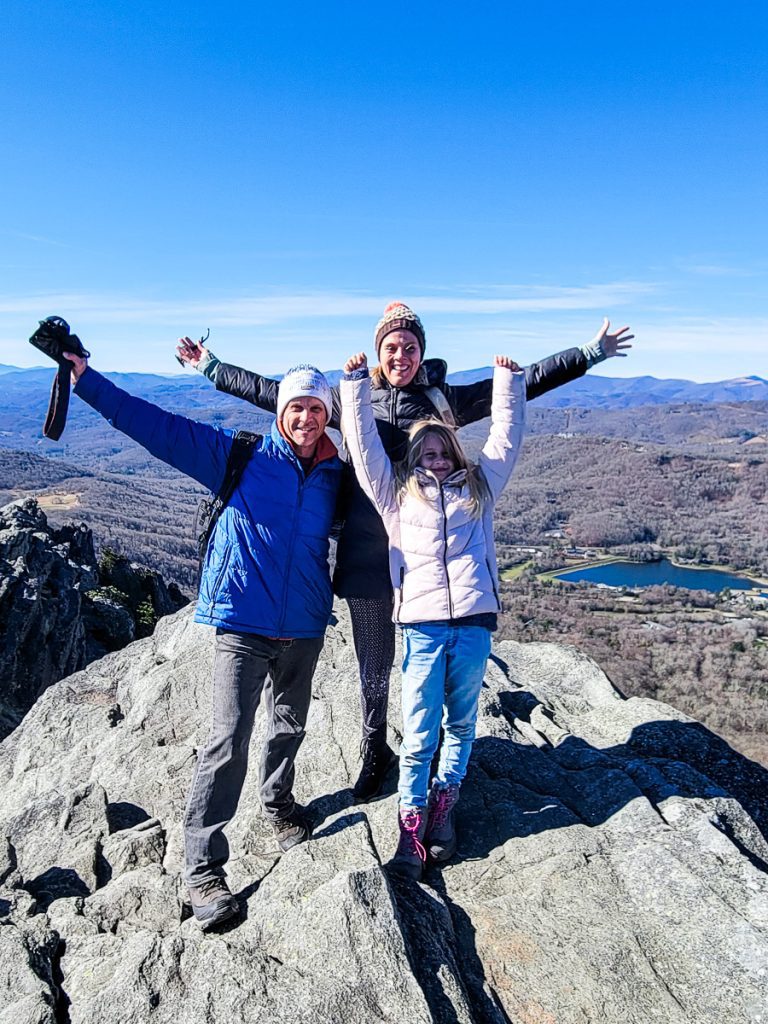 Three people standing on a rock ledge with arms raised