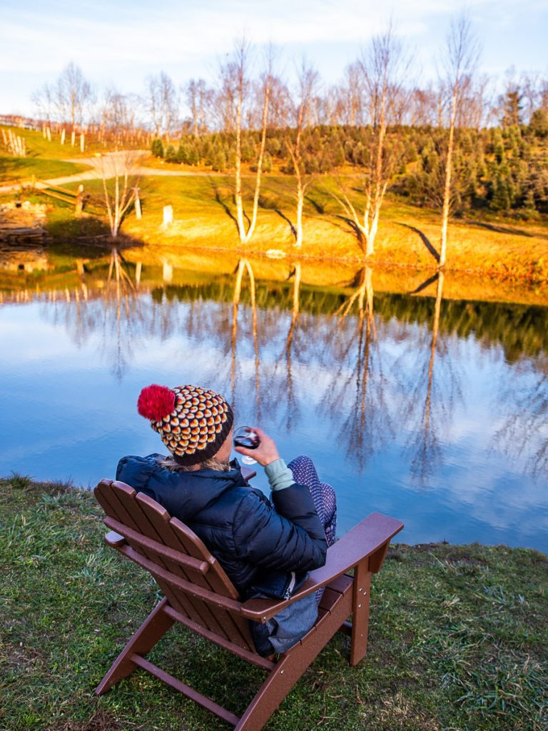 Lady sitting in chair overlooking pond drinking wine