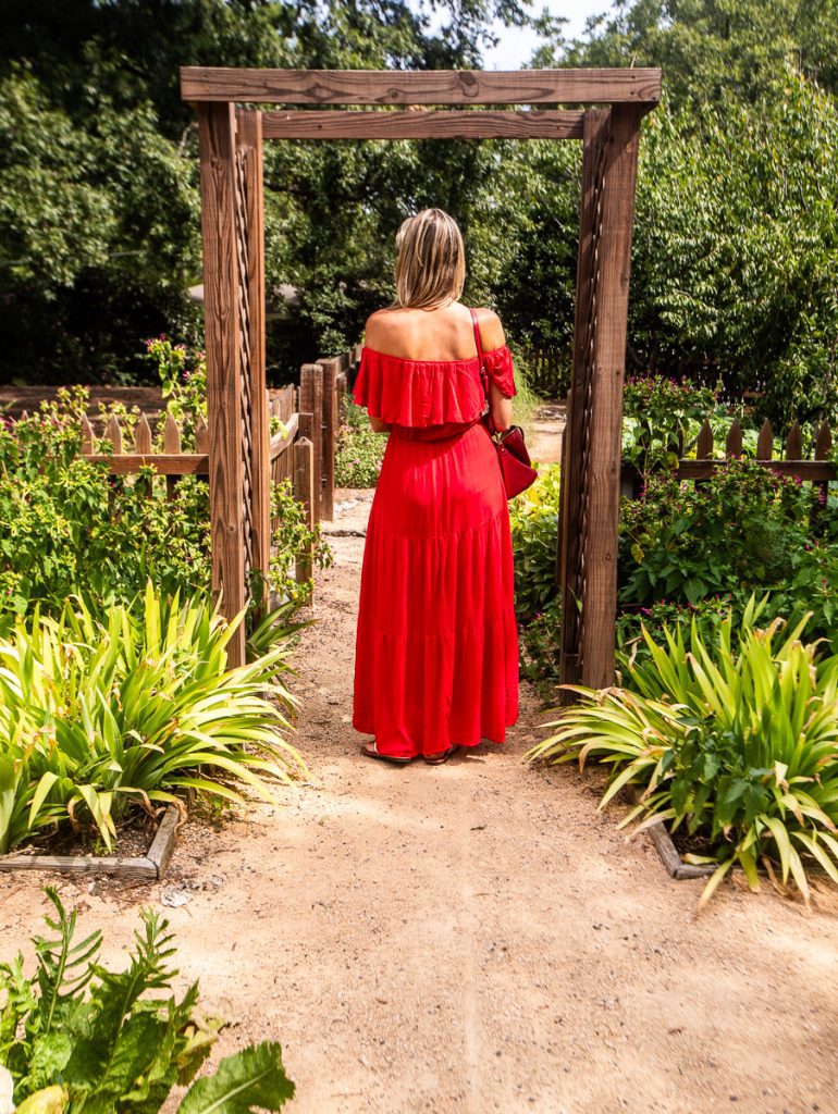 Lady in red dress walking through wooden entrance frame to a garden