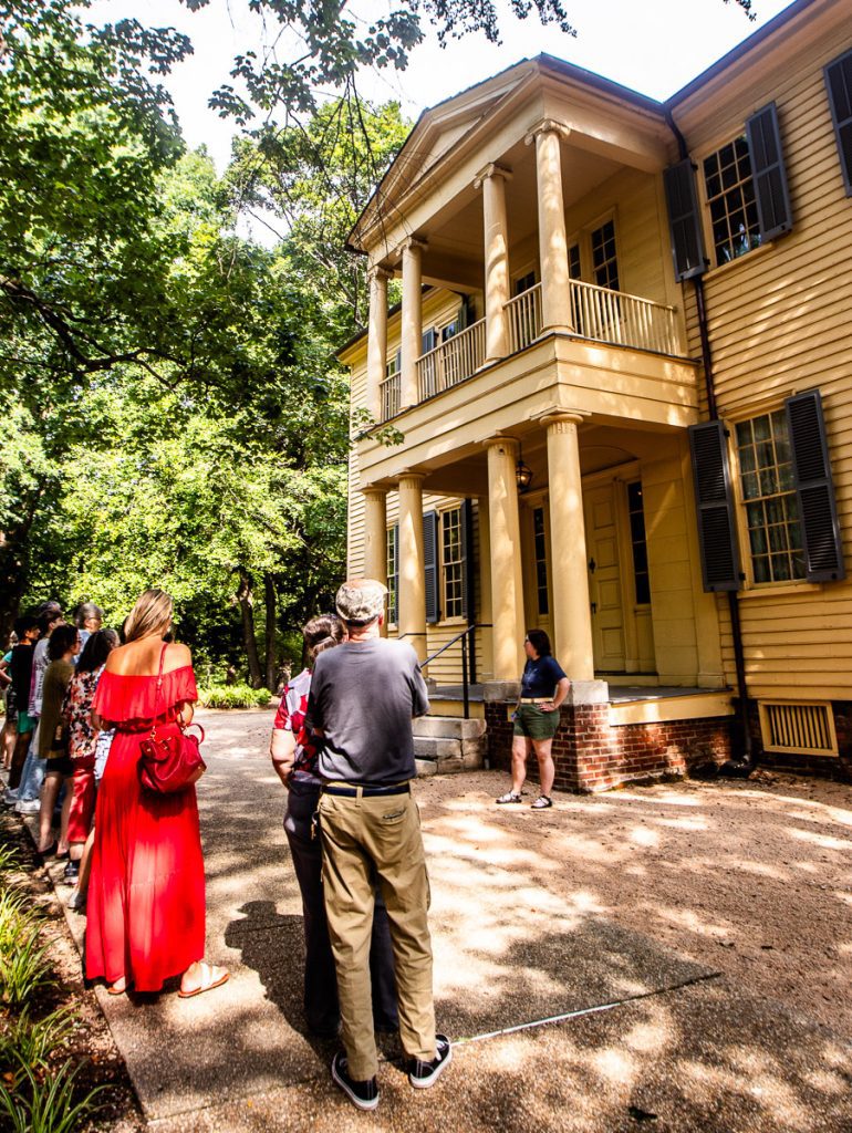 People standing outside a yellow historic Southern home