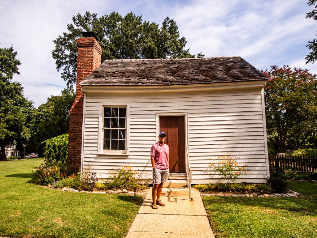 Man in pink shirt standing in front of a white cottage