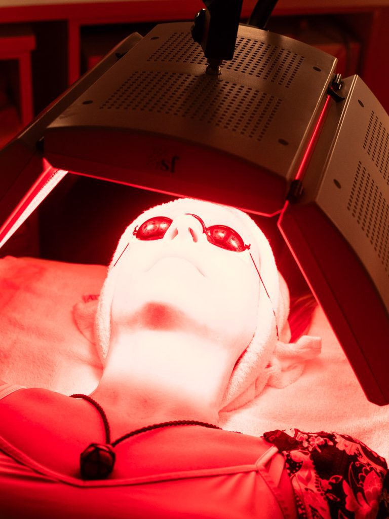 A woman lying down receiving red light therapy to her face.
