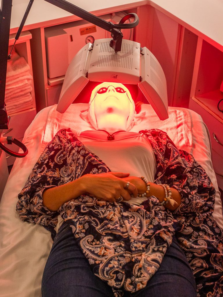 A woman lying down receiving red light therapy to her face.