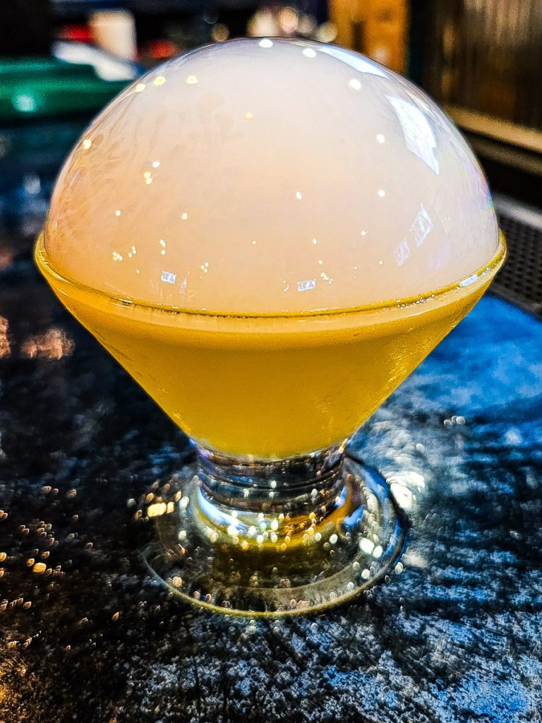 A yellow cocktail with a white bubble on top.