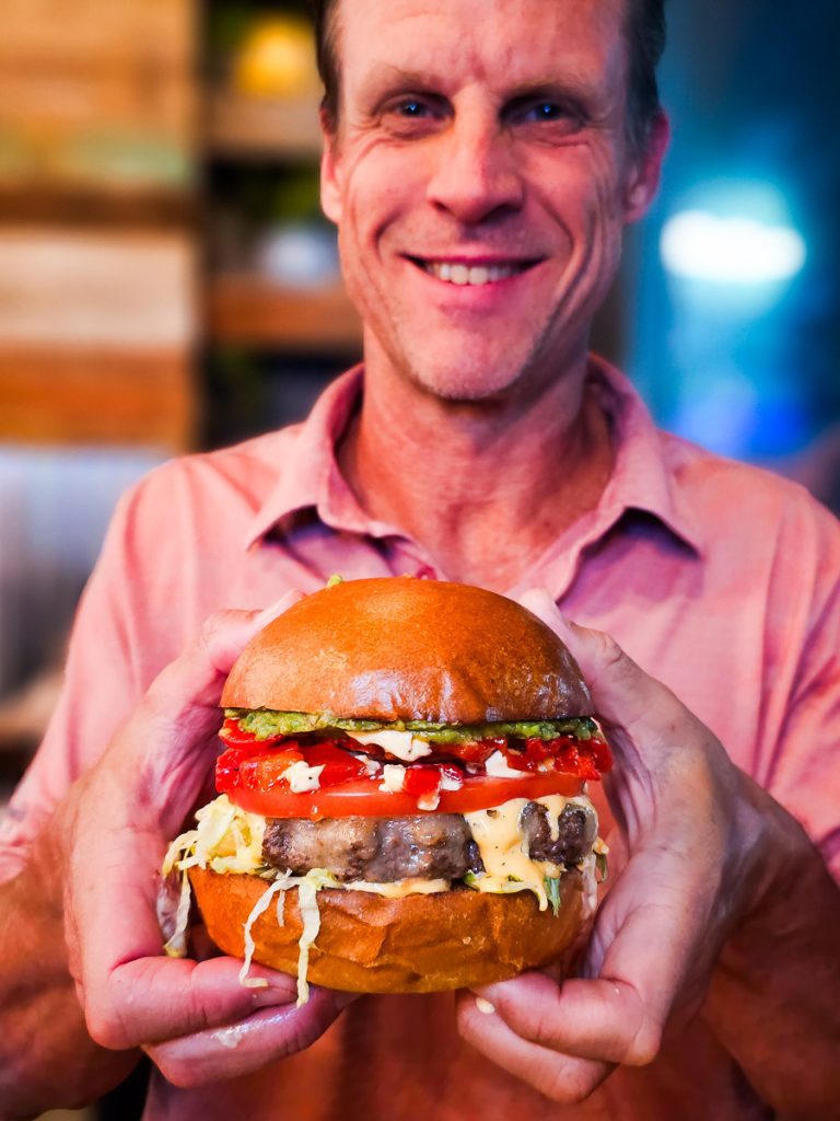 Man holding up a burger in his hands and smiling.